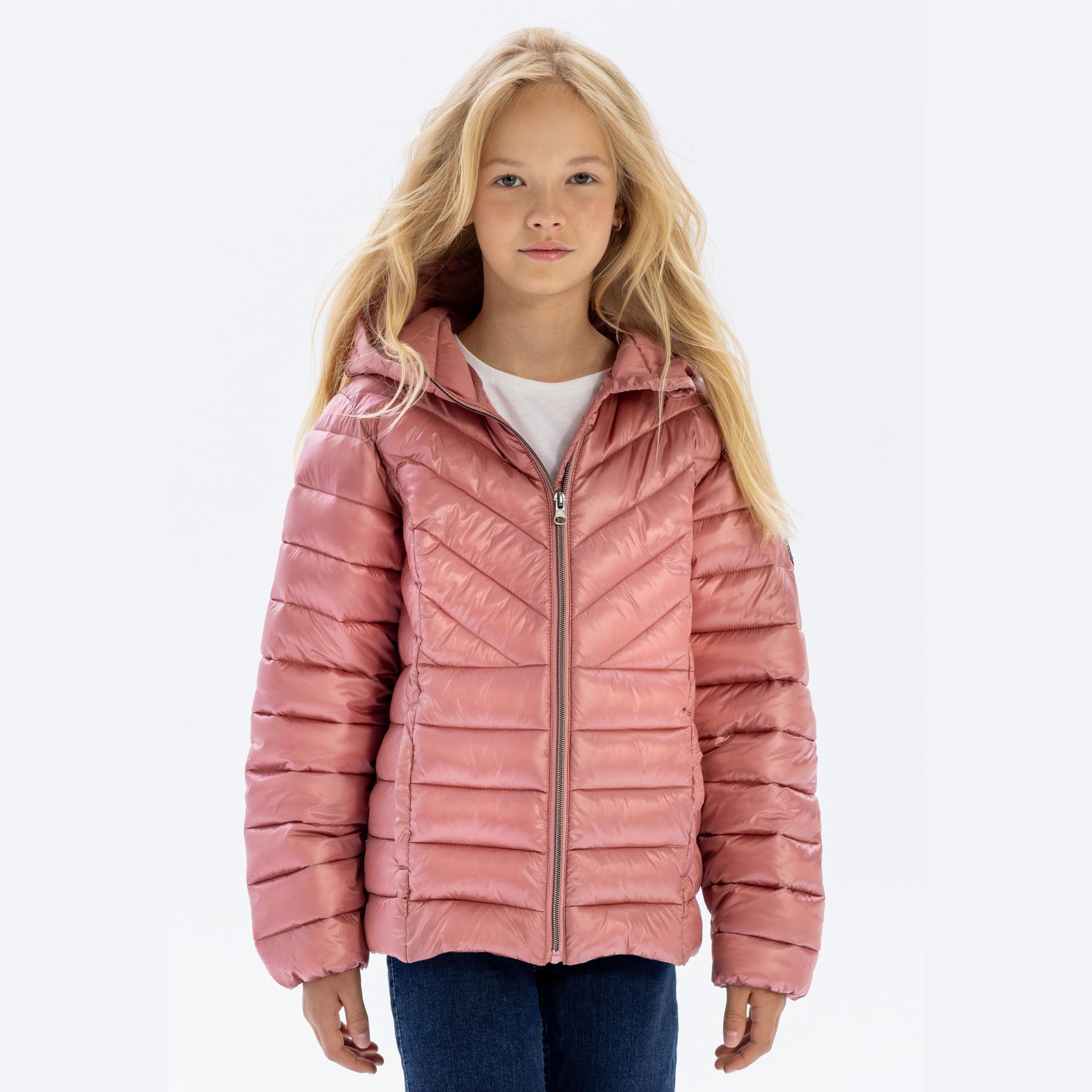 Young girl wearing copper quilted hooded jacket with zip closure over white top and jeans, standing against light background