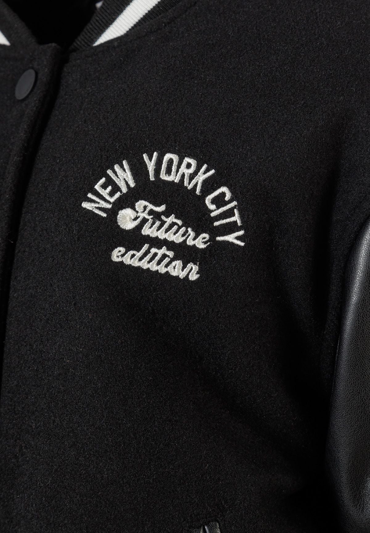 Close-up of the chest lettering on the black varsity jacket.