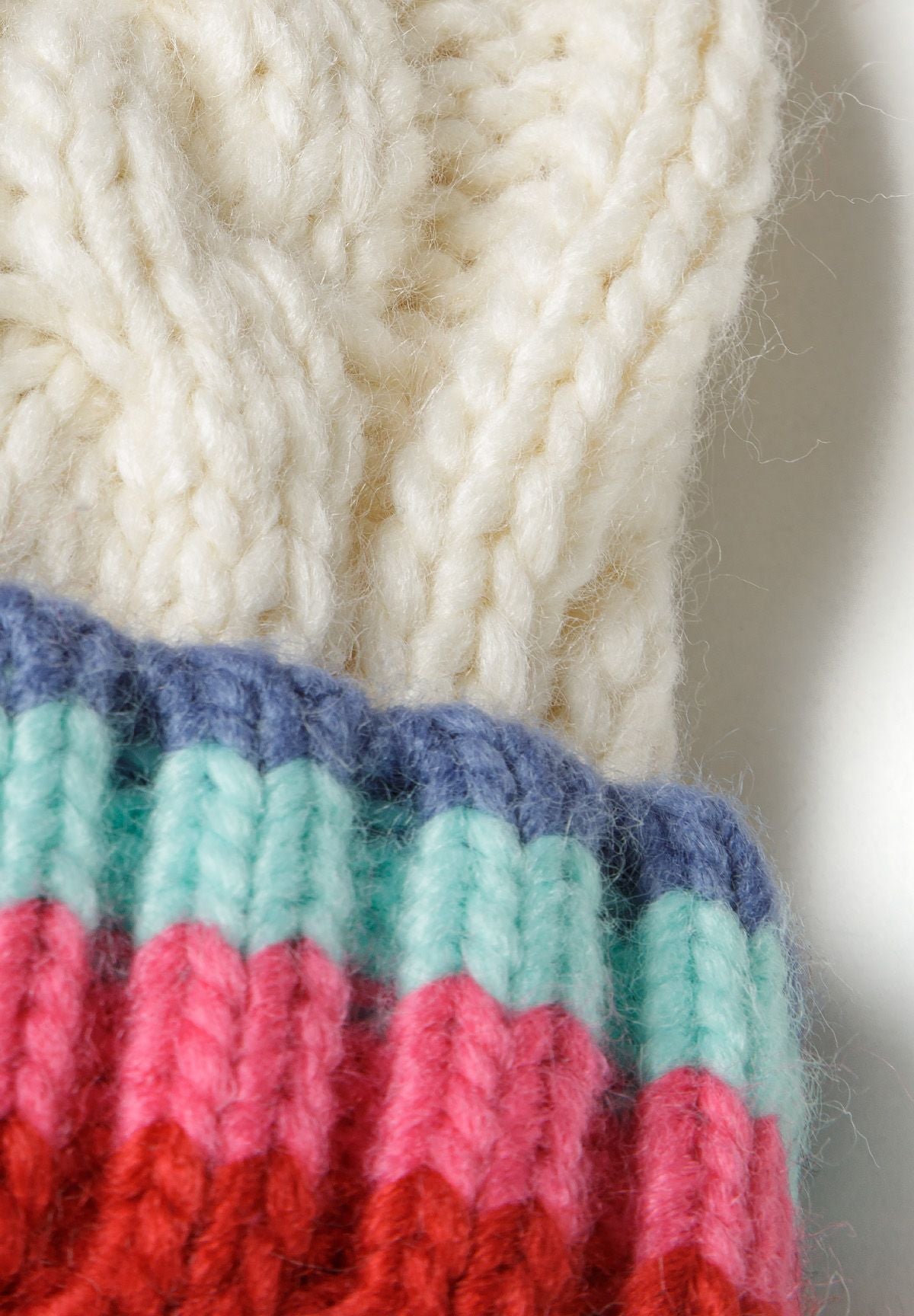 Detail of a cream knitted hat with a pom pom and colorful striped gloves.
