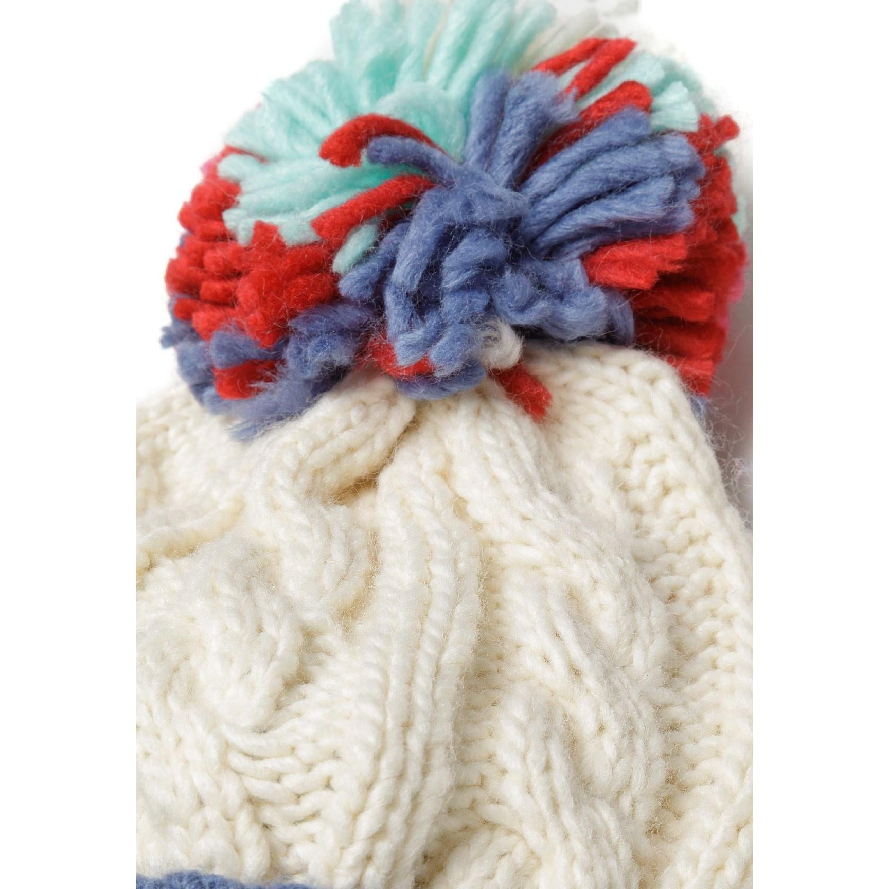 Detail of colourful pom pom in red, blue, mint and cream colours attached to cable knit hat