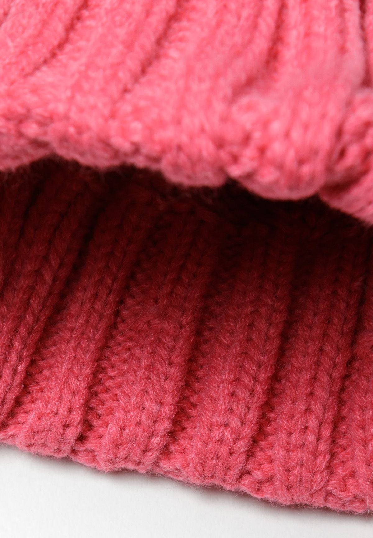 Bright pink cable-knit bobble hat, inside turn-up.