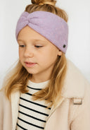 Close-up of a light pink headband with a front twist and a small metal badge.