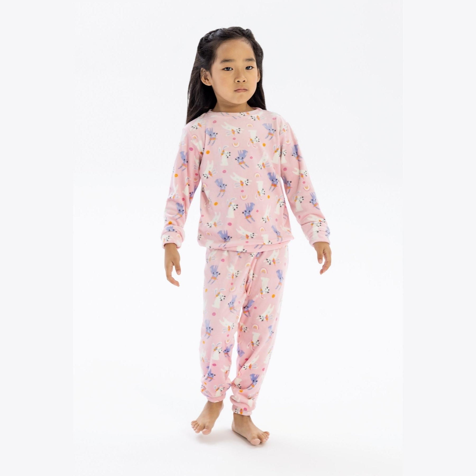 Young girl wearing pink velour pyjama set with unicorn print, standing against white background