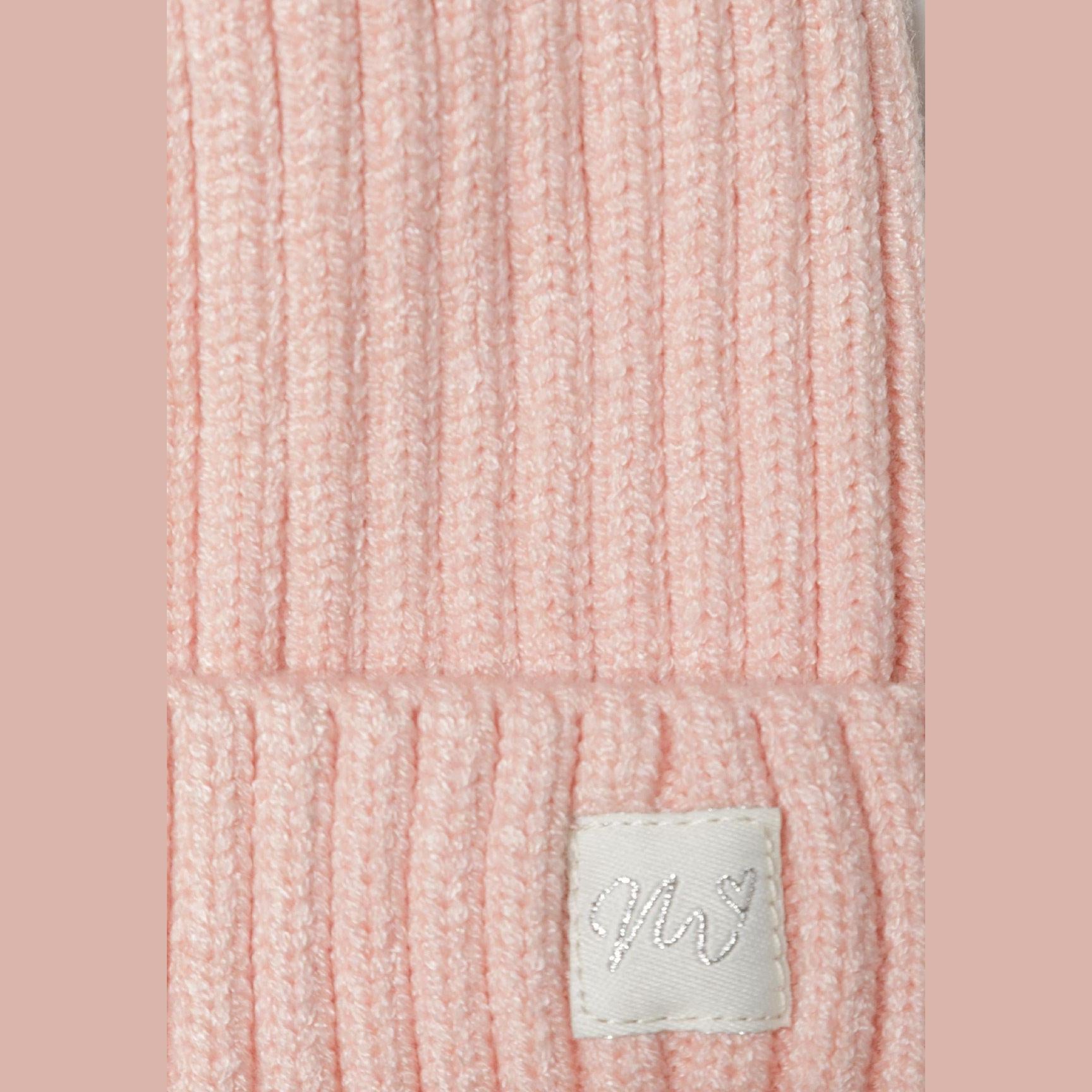 Close-up detail of light pink ribbed knit texture showing fold-up brim with white lurex badge on pink background