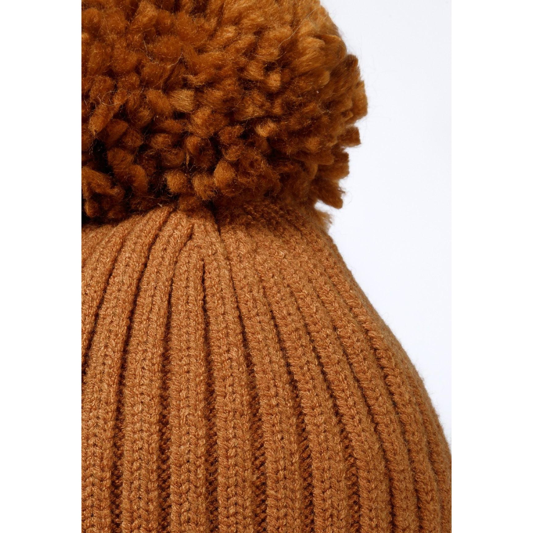 Close-up detail of beige knitted hat showing ribbed texture and fluffy pom pom construction