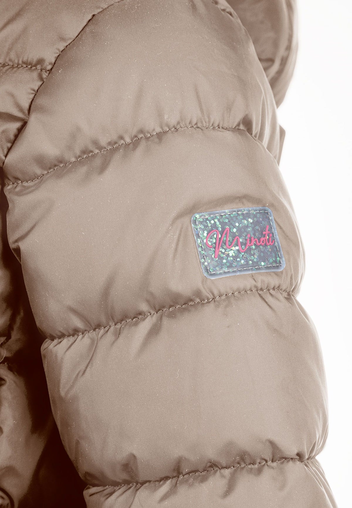 Close-up of an iridescent Minoti patch on the beige jacket sleeve.