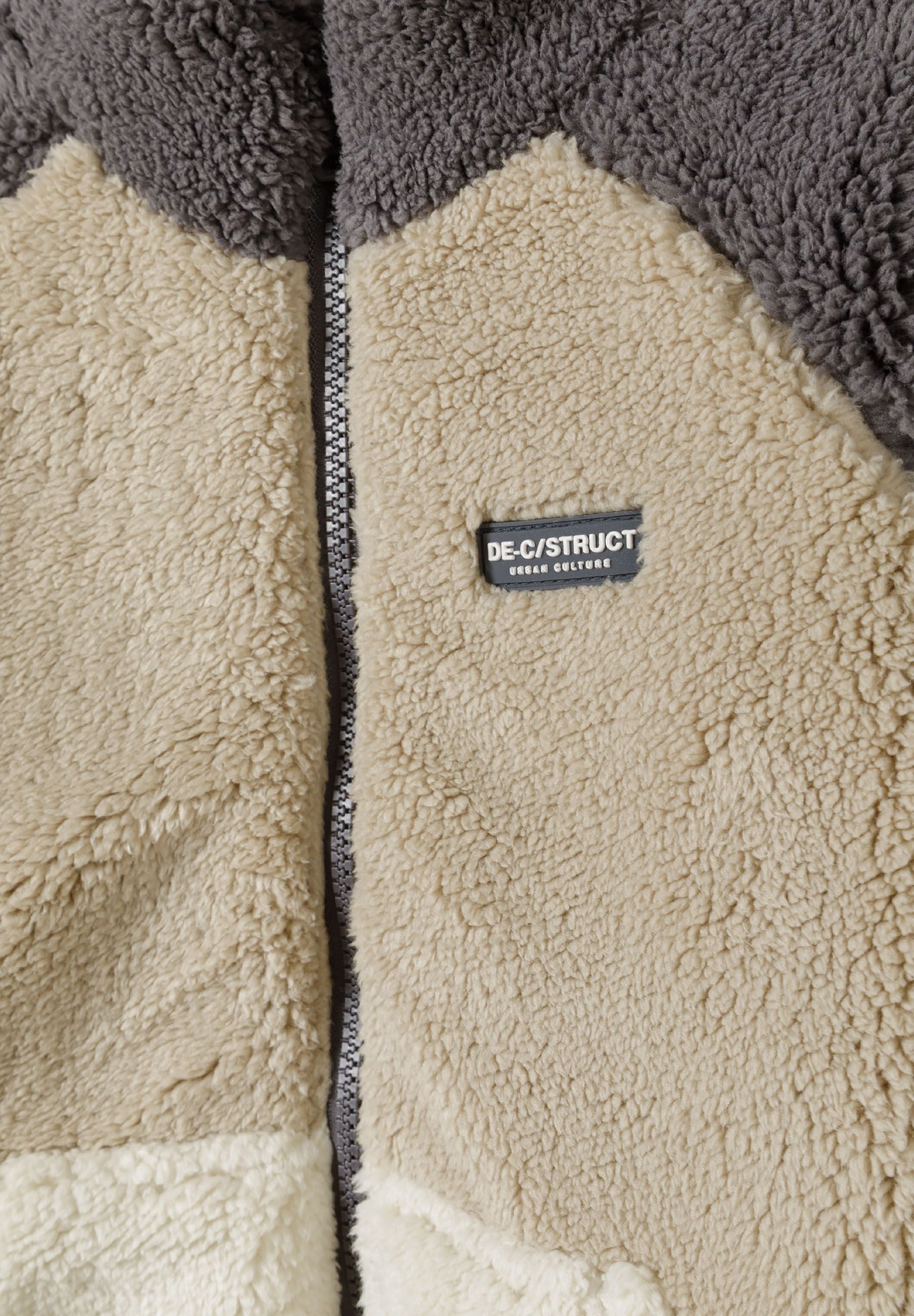Detail of boys sherpa fleece jacket with cream pocket and chest badge.