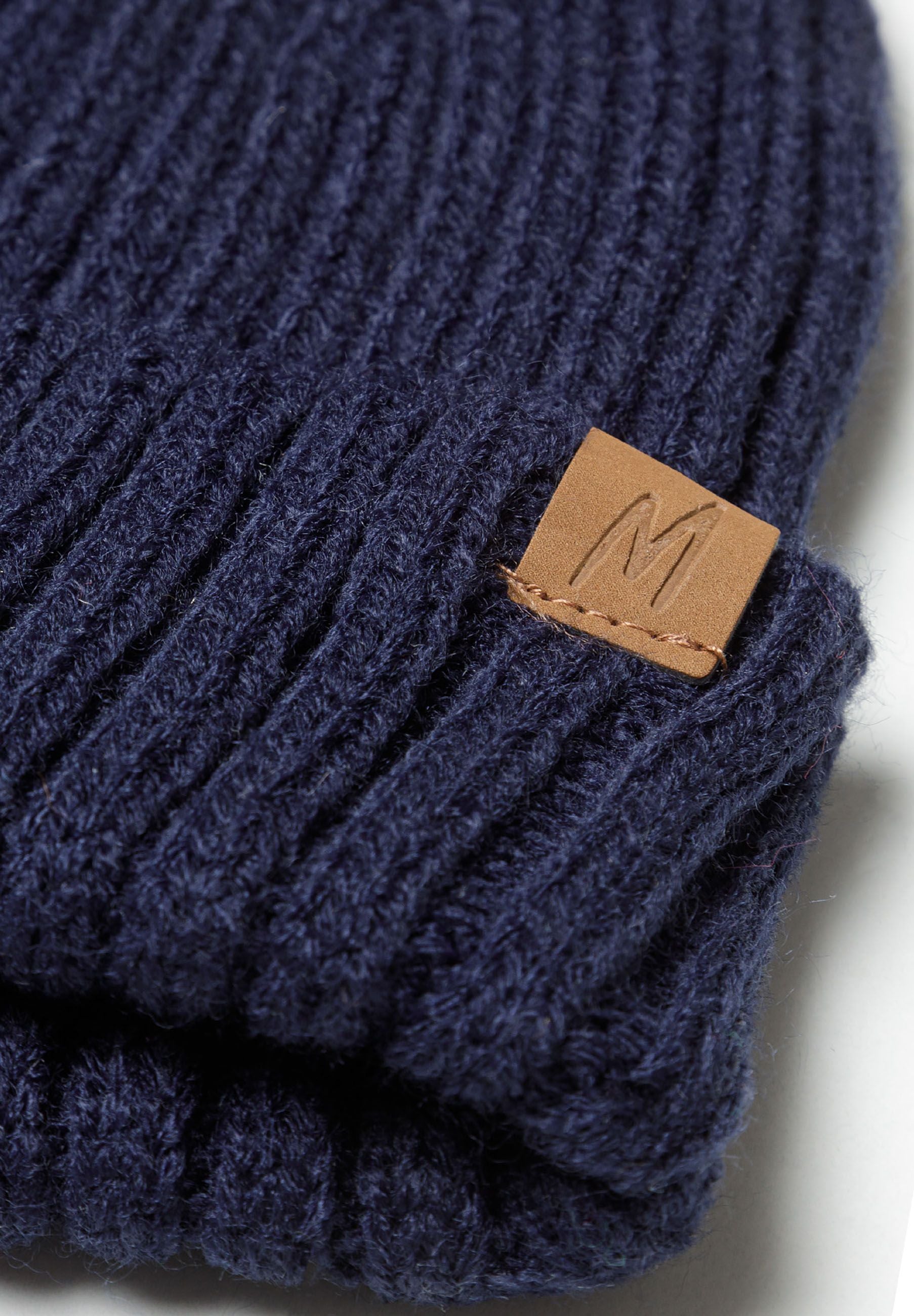Detail of navy ribbed beanie with leather logo patch.