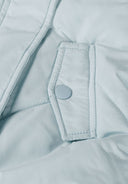 Detail of a light blue padded baby jacket with a snap button and zig-zag quilting.