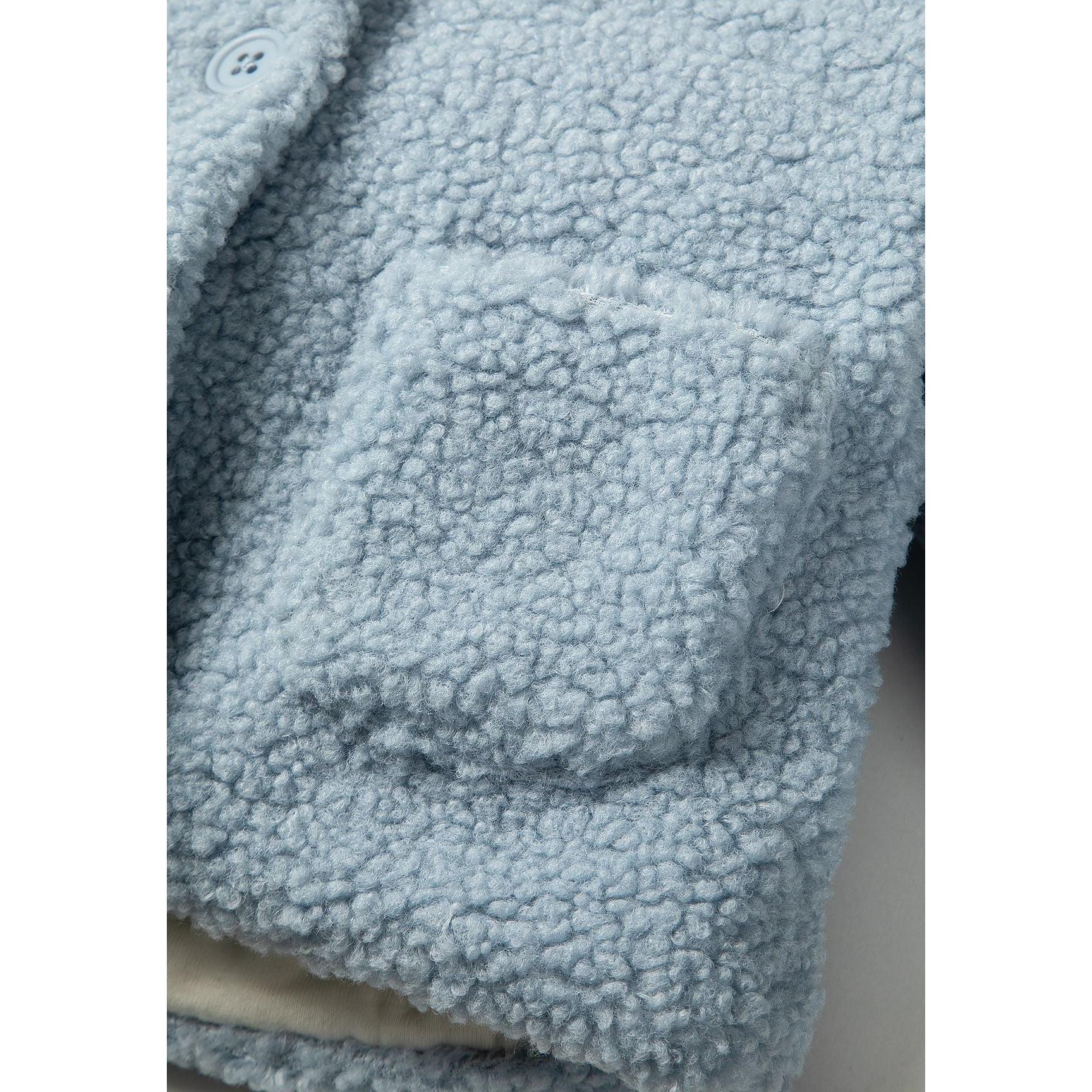 Detail view of light blue teddy fleece texture and front pocket construction of baby jacket