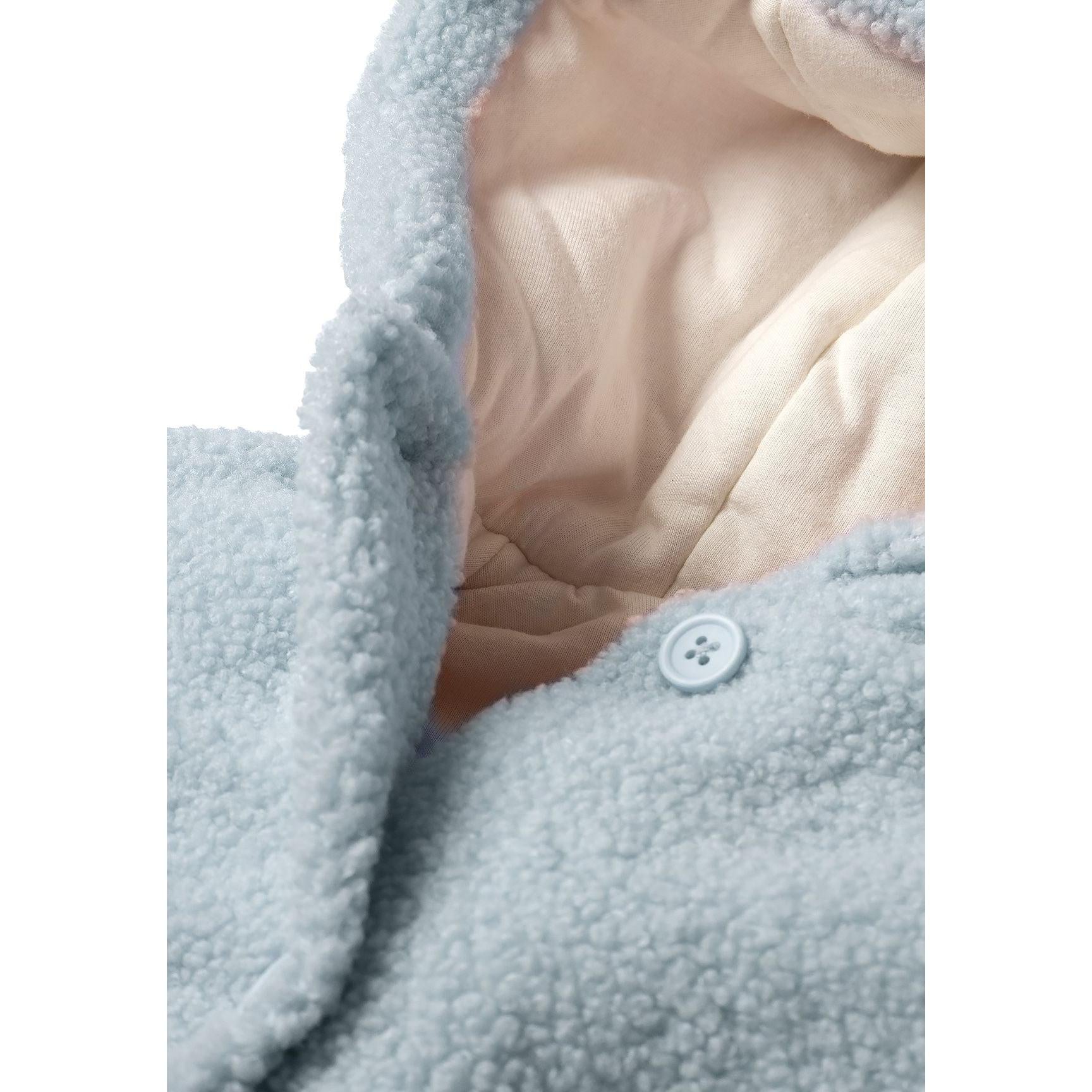 Close-up detail of light blue teddy fleece jacket showing cream jersey lining interior and button fastening mechanism