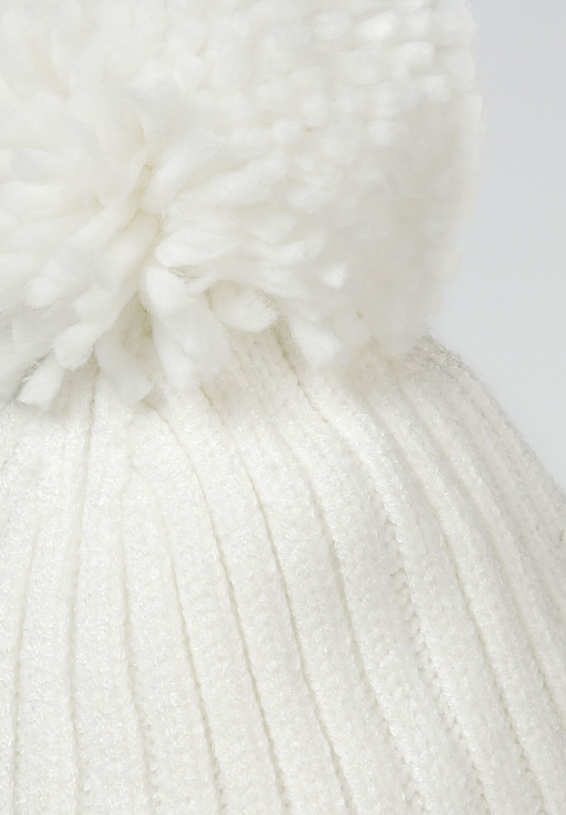Detail of a cream ribbed knit hat with a pompom on top.