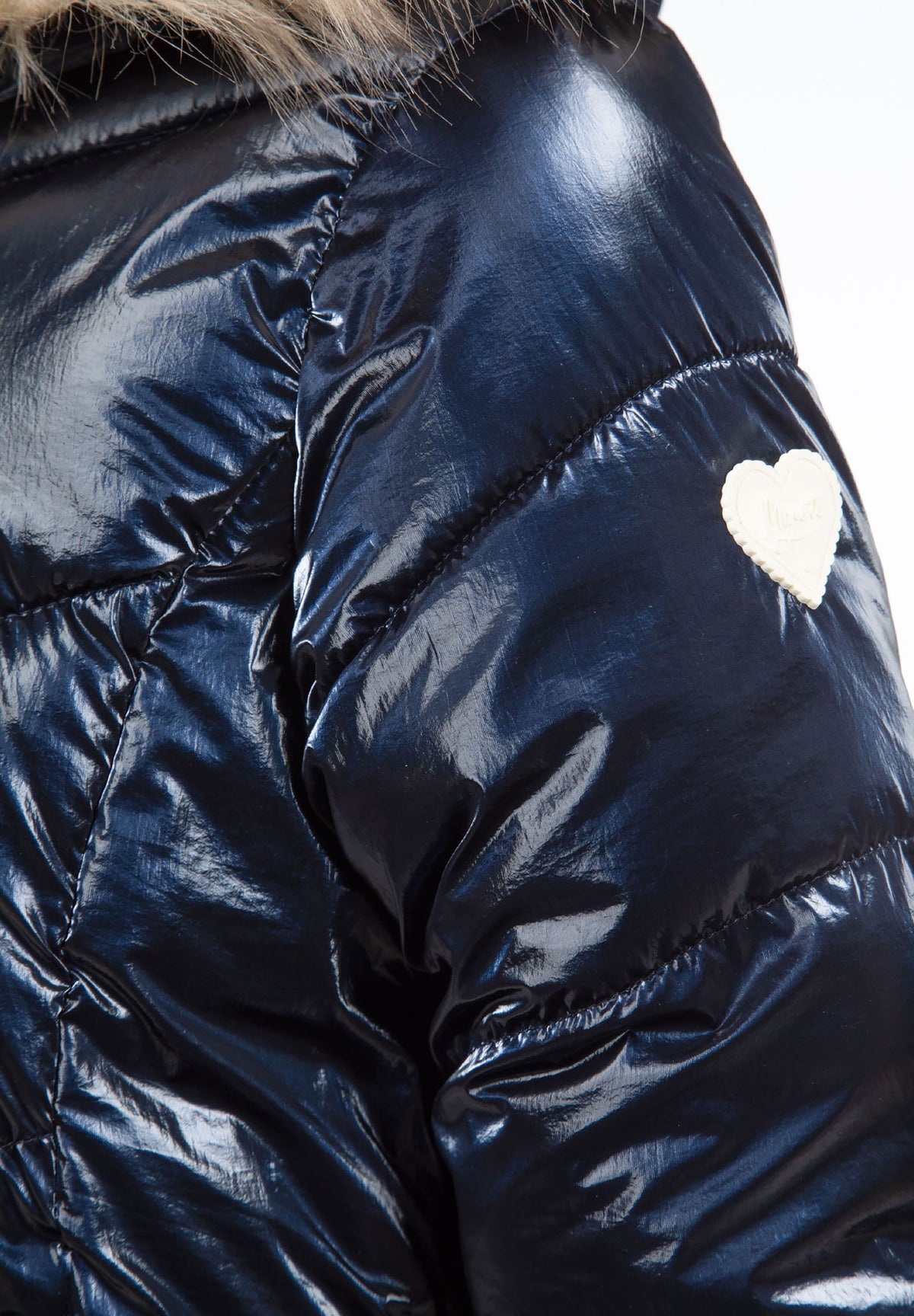 Close-up of a cream heart-shaped badge on the glossy navy puffer jacket sleeve.