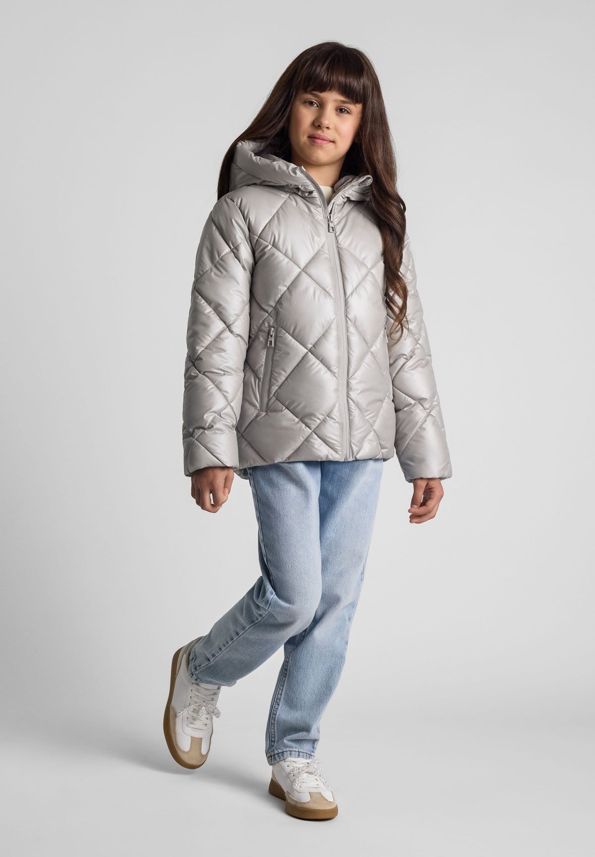 Child wearing a silver hooded puffer jacket with diamond quilting and zipped pockets.
