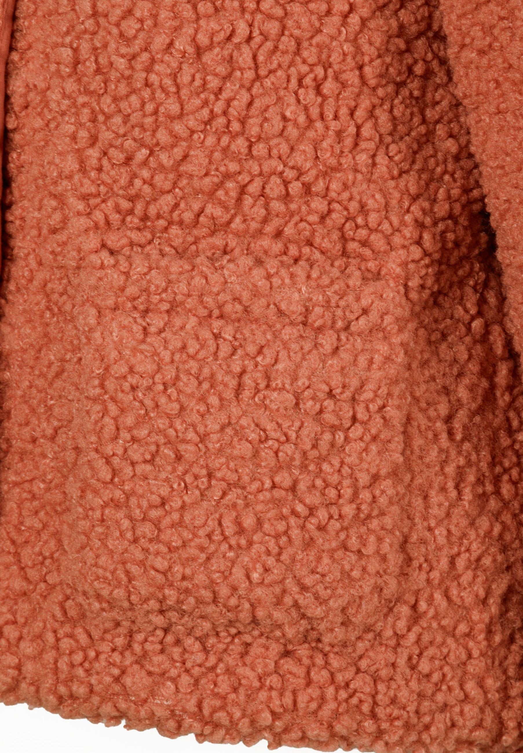 Detail of a teddy fleece jacket in soft pink with a textured surface and a front patch pocket.