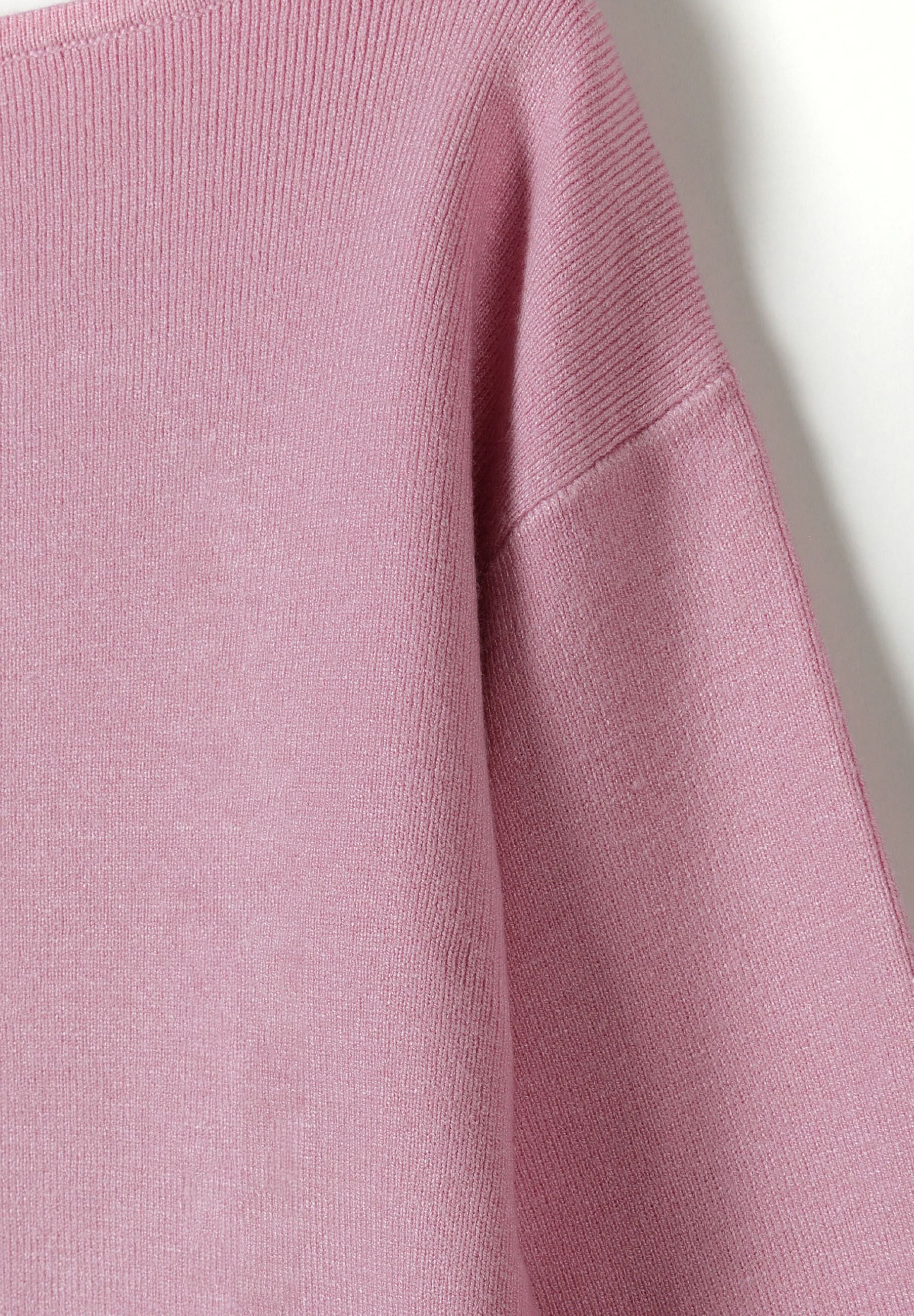 Detail of a girls' pink jumper with a boat neckline and ribbed cuffs.