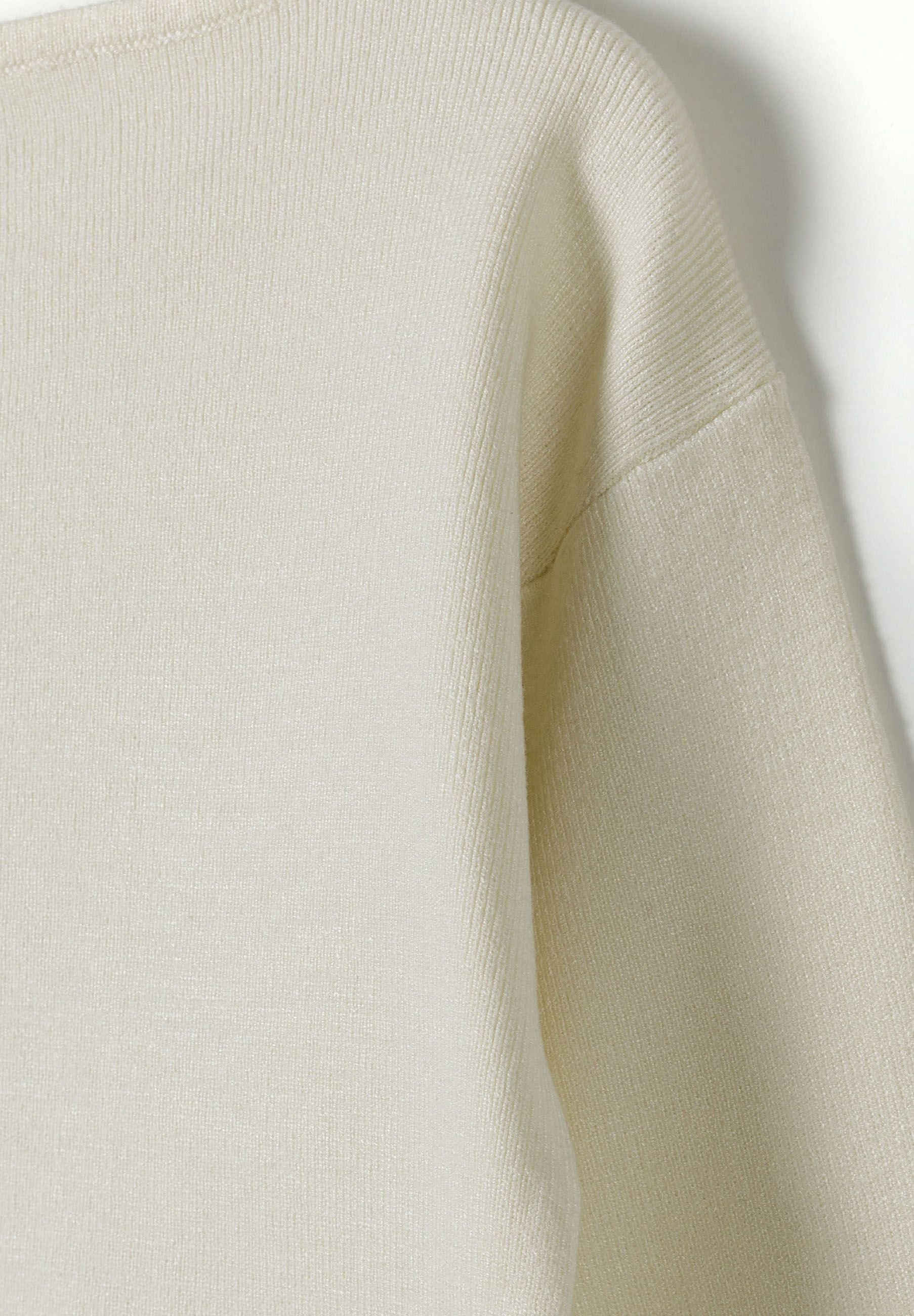 Detail of a cream girls jumper with a boat neckline and ribbed cuffs.