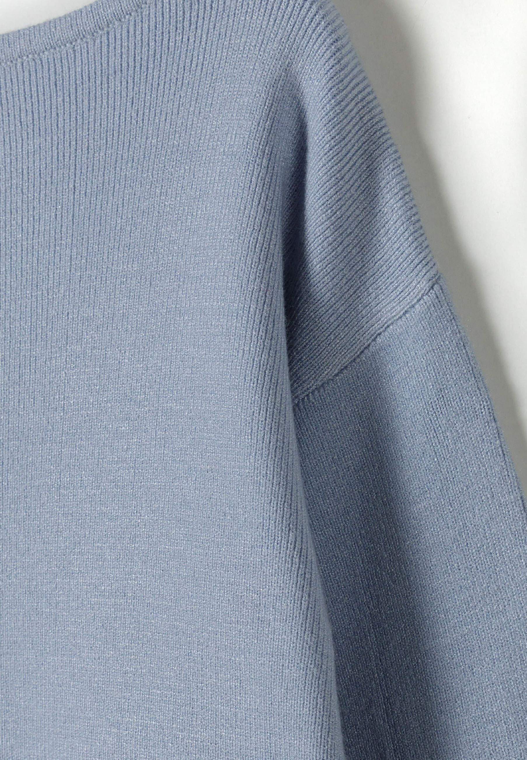 Detail of a light blue girls jumper with a boat neckline and ribbed cuffs.