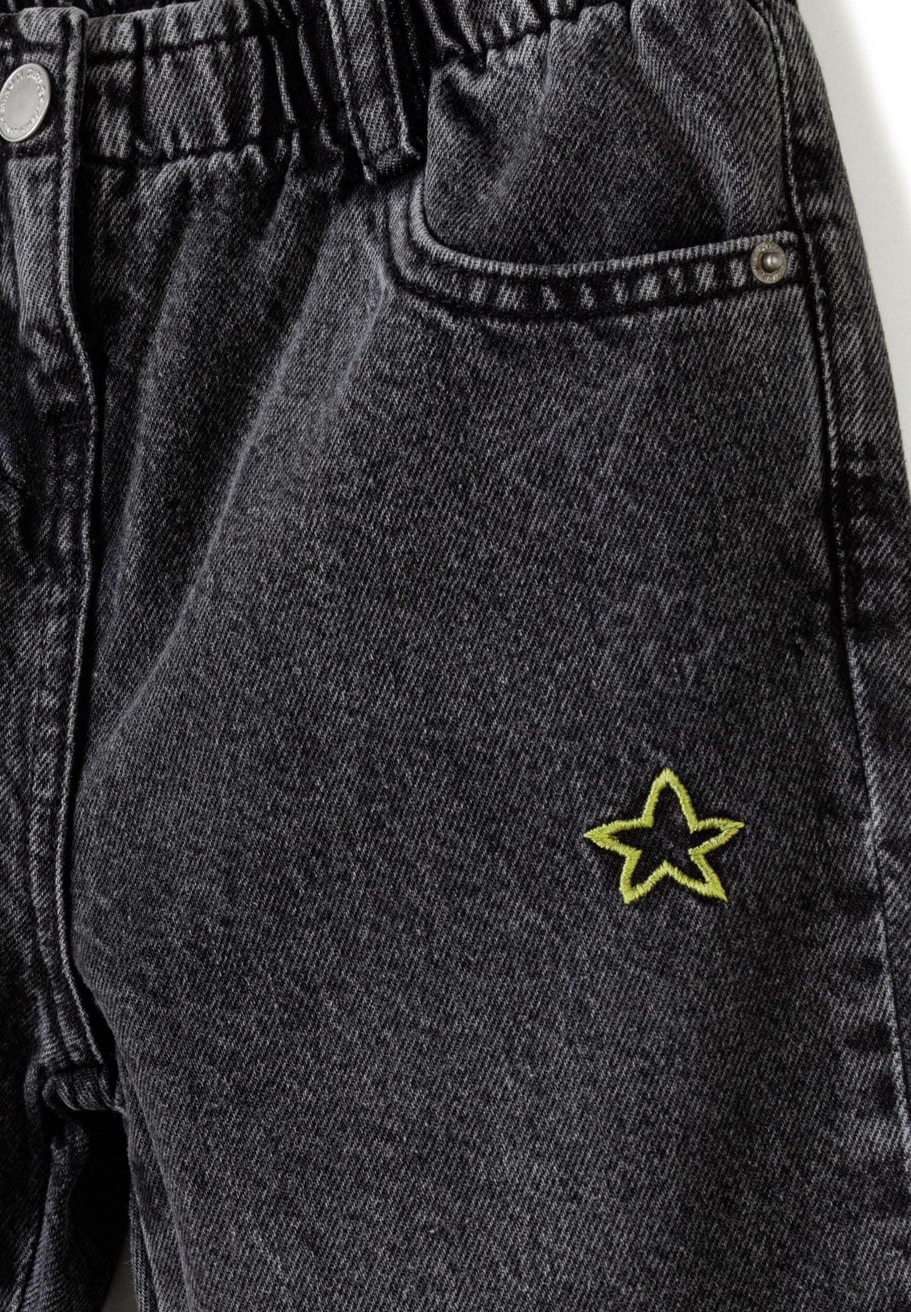 Close-up of girls' black jeans with elasticated waist and star embroidery.
