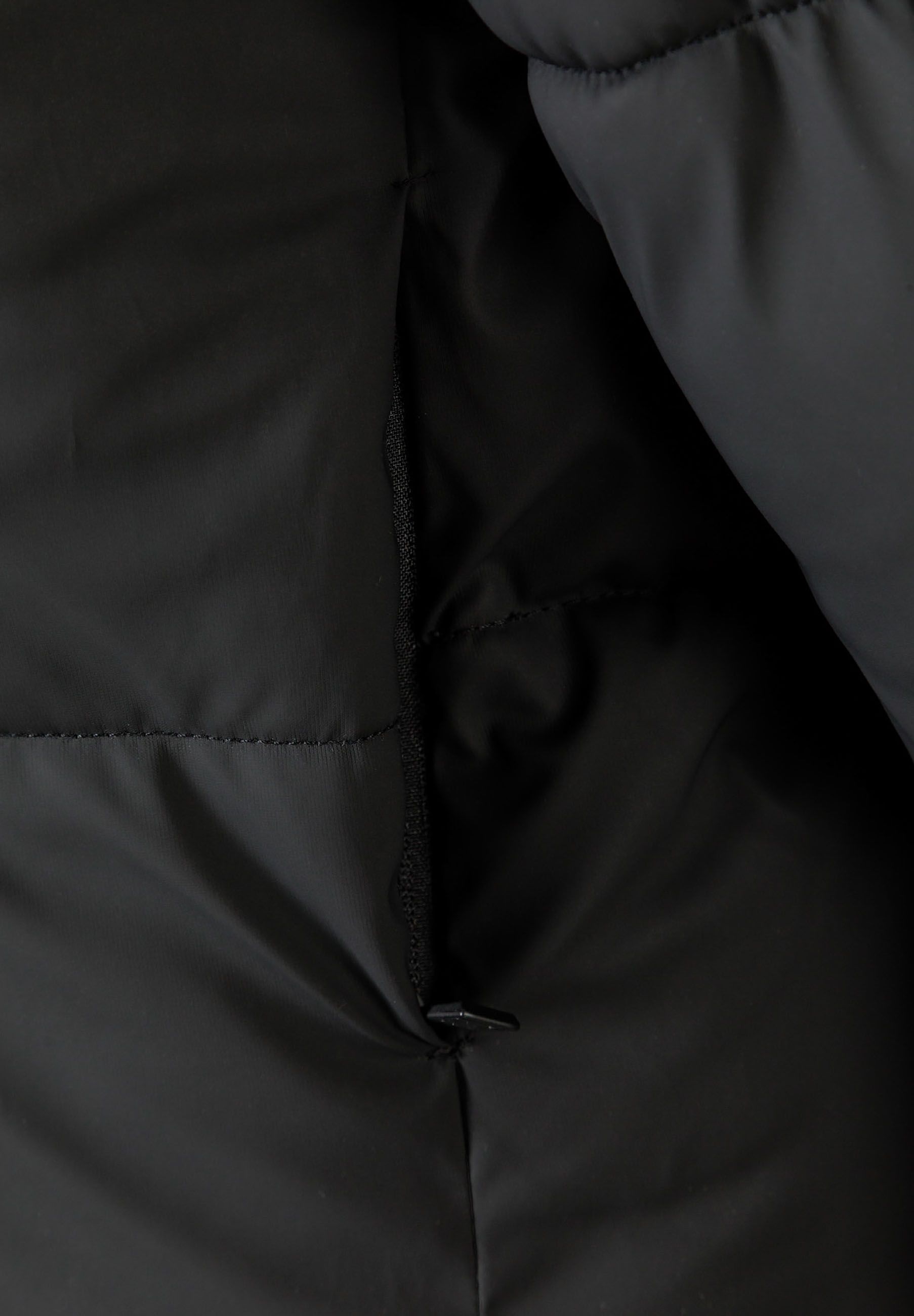 Detail of a black short quilted jacket with hood and high collar.