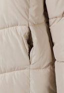 Detail of a long quilted winter jacket featuring side pockets and thick padding.