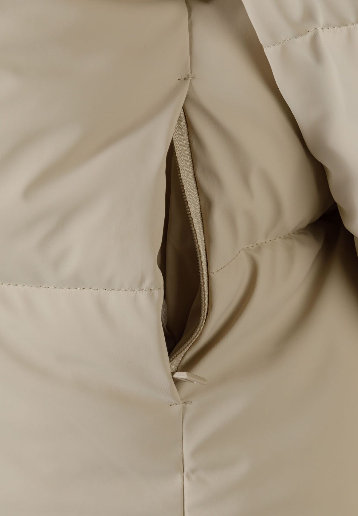 Close-up of the pocket on the beige cropped puffer jacket.