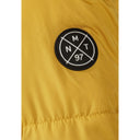 Close-up of a mustard boys' jacket sleeve with a round black and white branded badge.