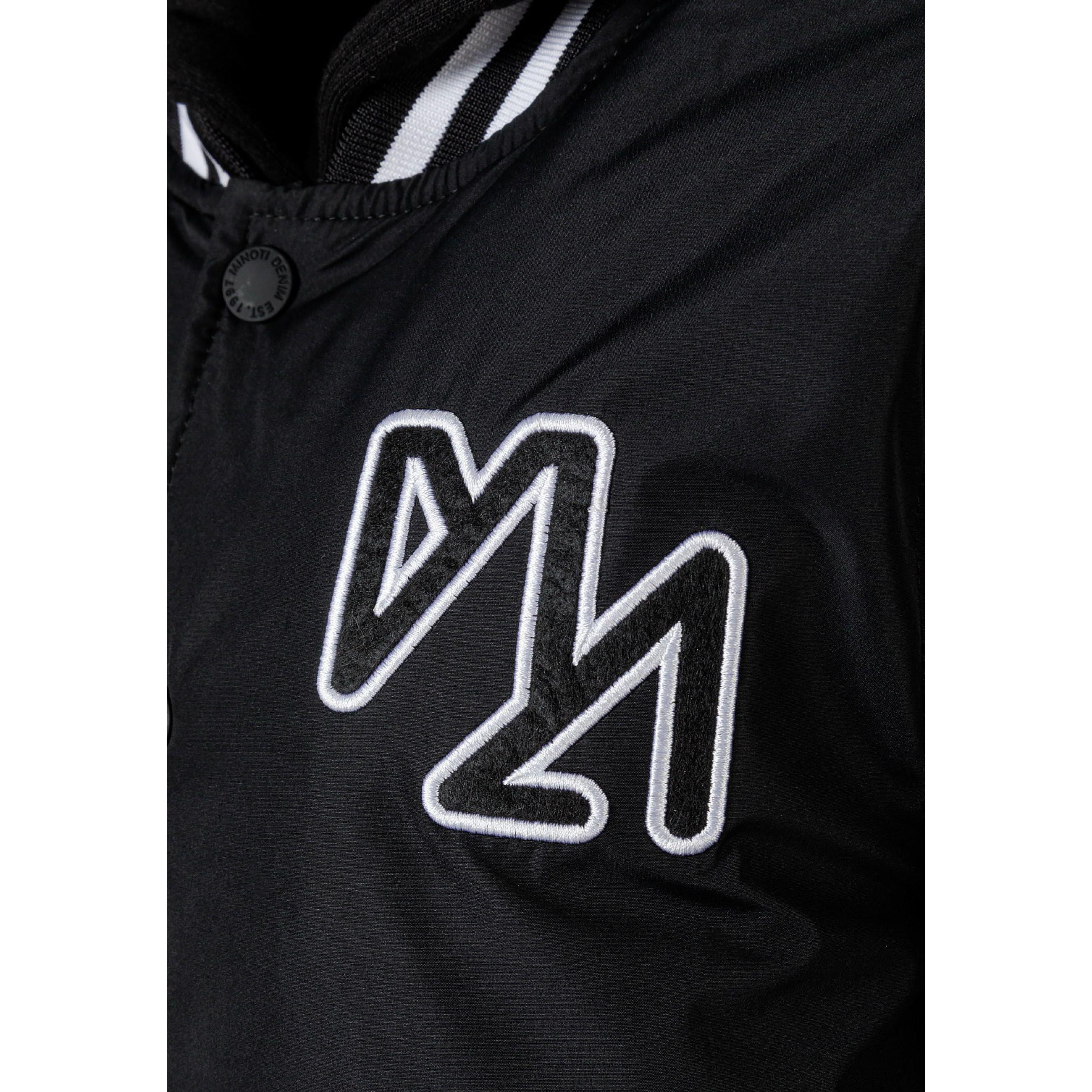 Close-up detail of black baseball jacket showing white embroidered logo and snap button closure with striped ribbed trim