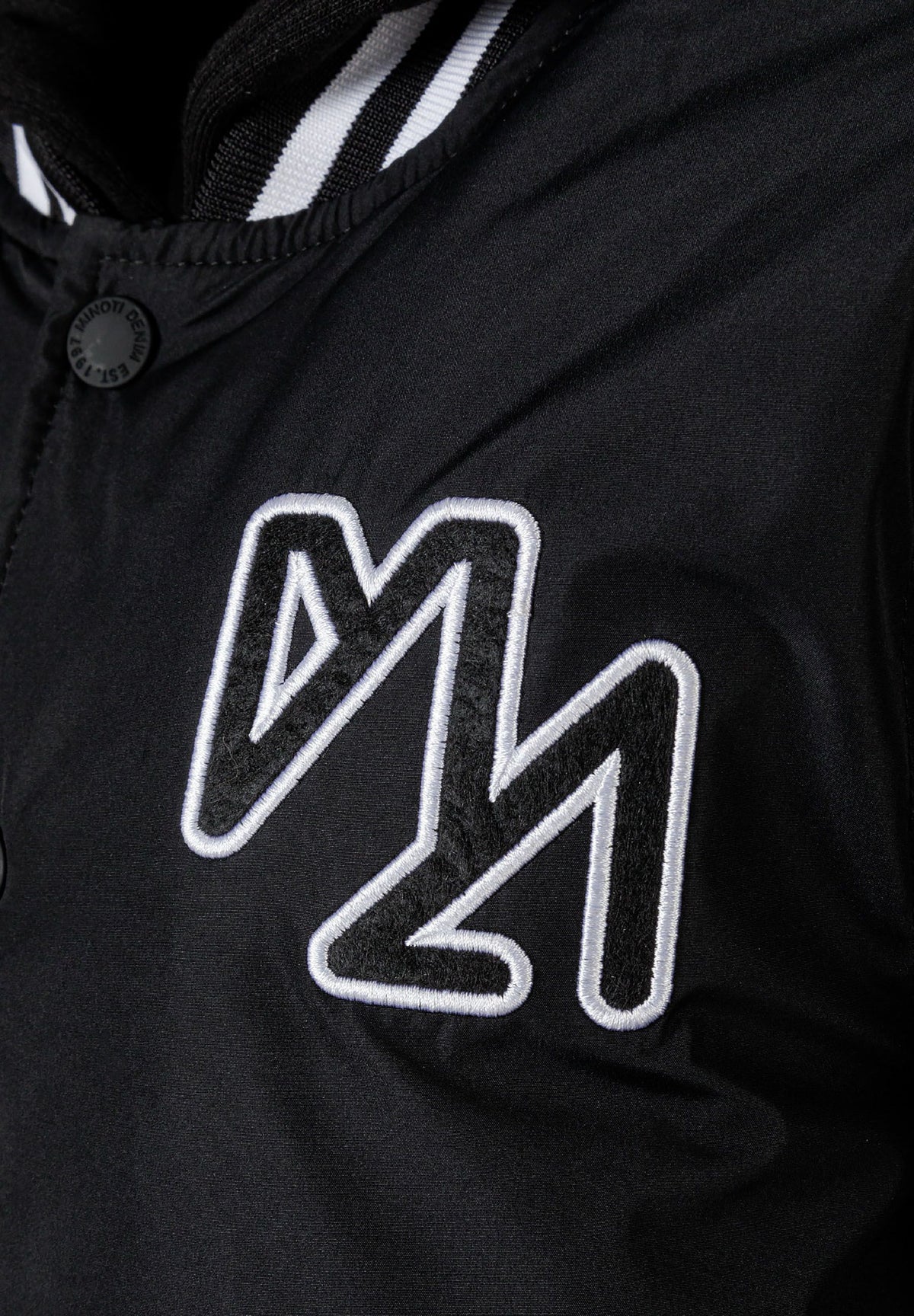 Close-up of the chest emblem on the black varsity jacket.