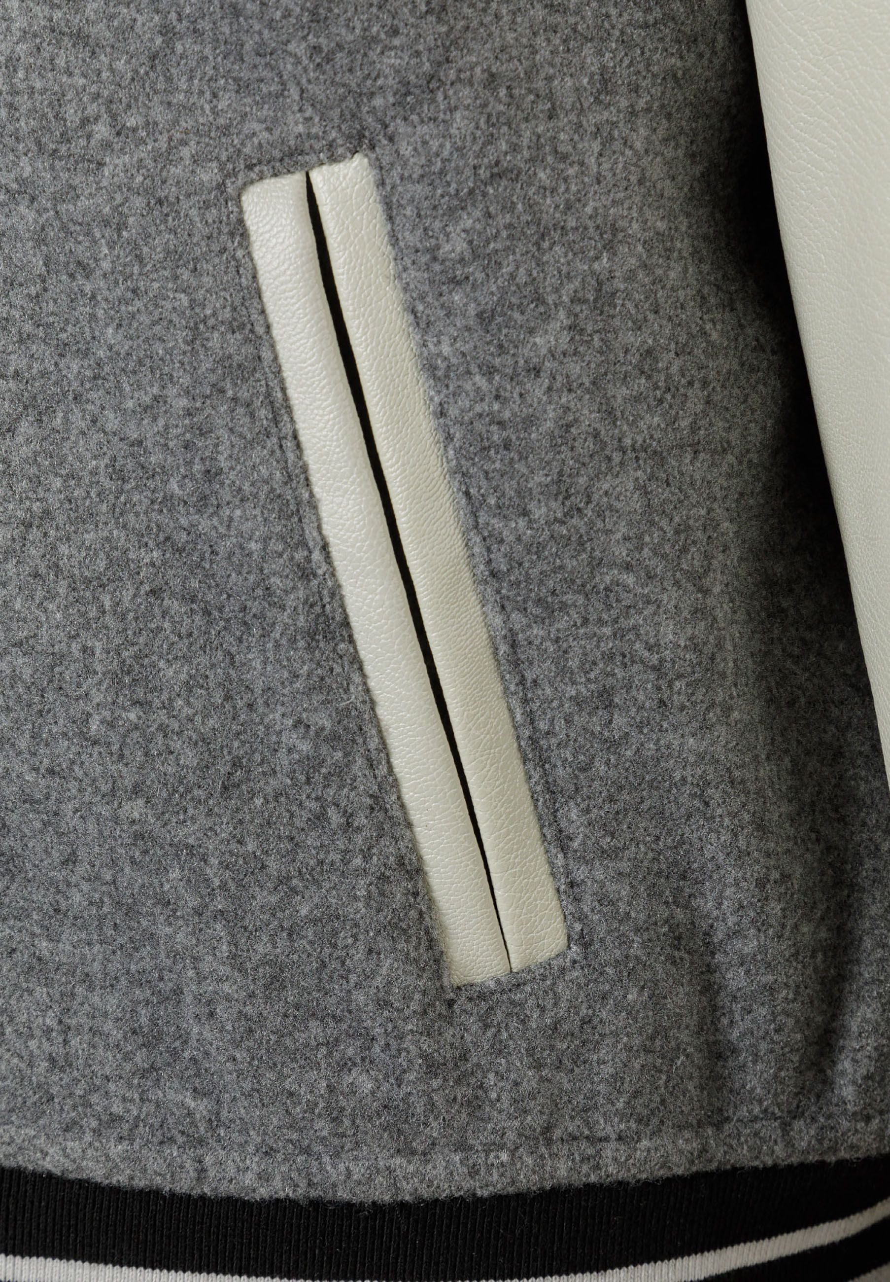 Detail of a boys varsity jacket showing grey fabric and PU sleeve with a side pocket.