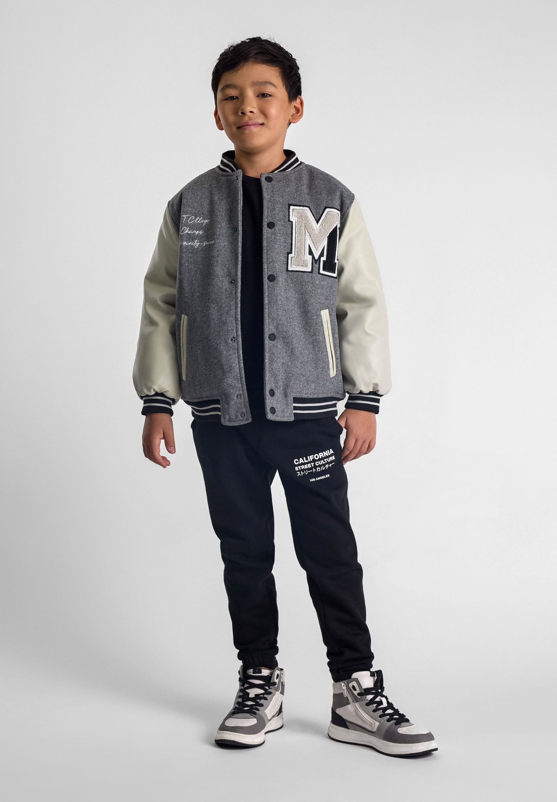 Boys varsity jacket in grey with snap buttons, quilted lining, and embroidered chest detail.