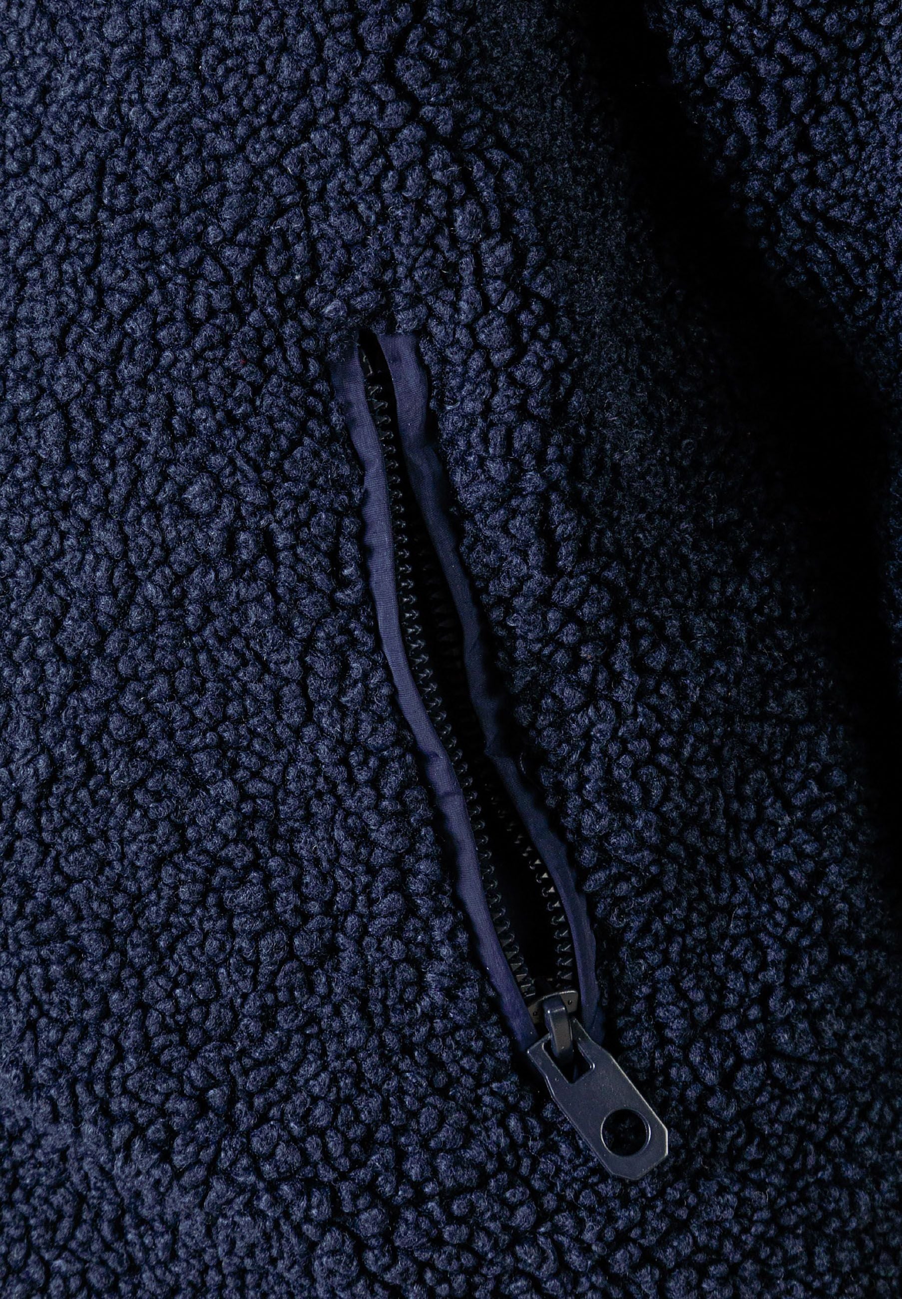 Detail of a navy boys padded borg jacket showing a zipped pocket.