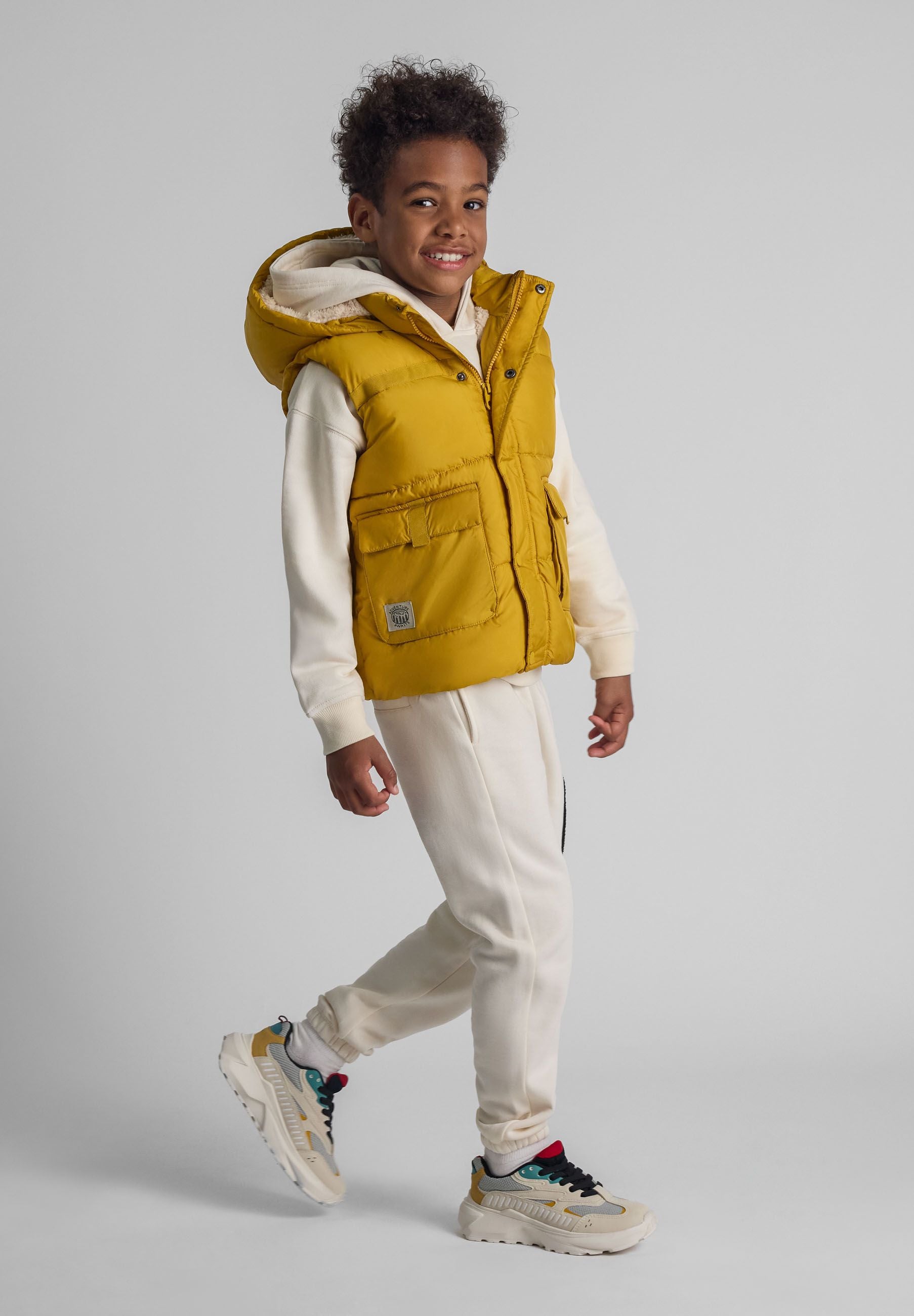 Boys mustard gilet with hood, two patch pockets, and zipper closure, side view.
