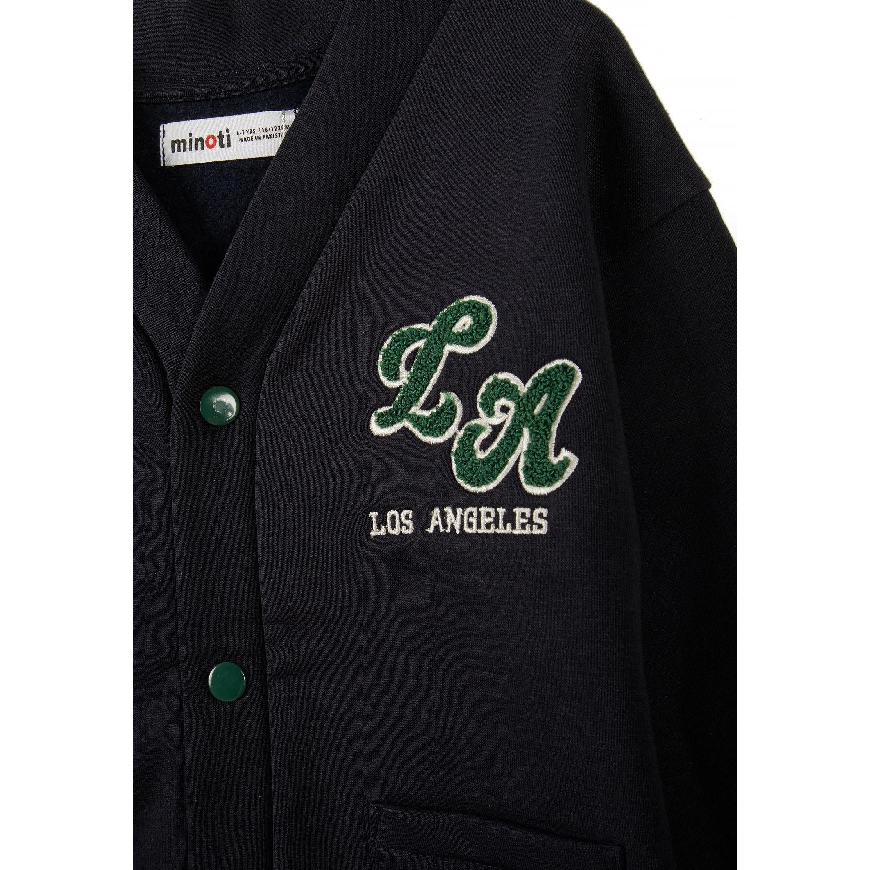 Close-up detail of navy cardigan showing LA Los Angeles embroidered applique, green buttons, and Minoti label inside collar