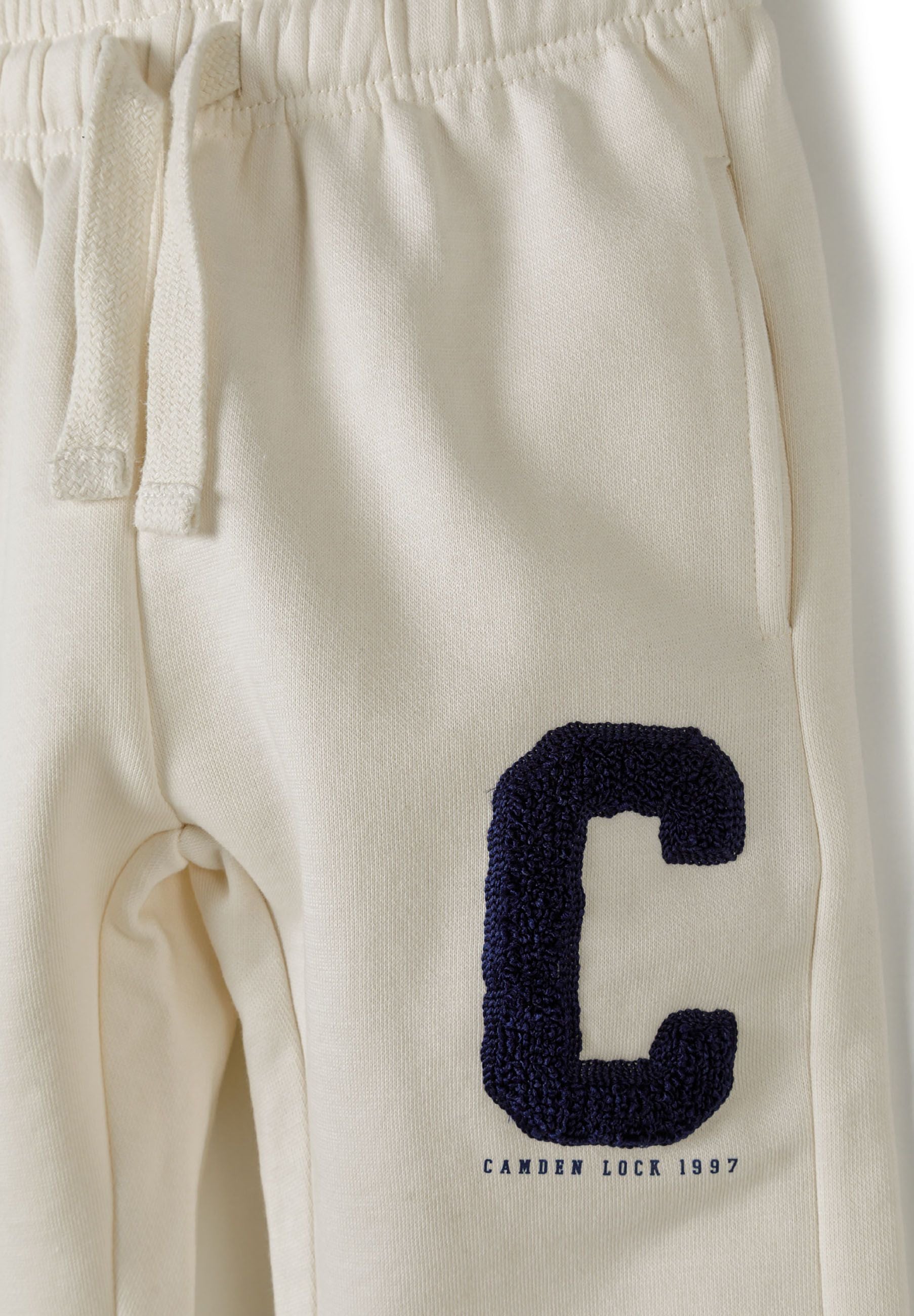 Detail of cream joggers with navy boucle 'C' embroidery and elastic waistband.