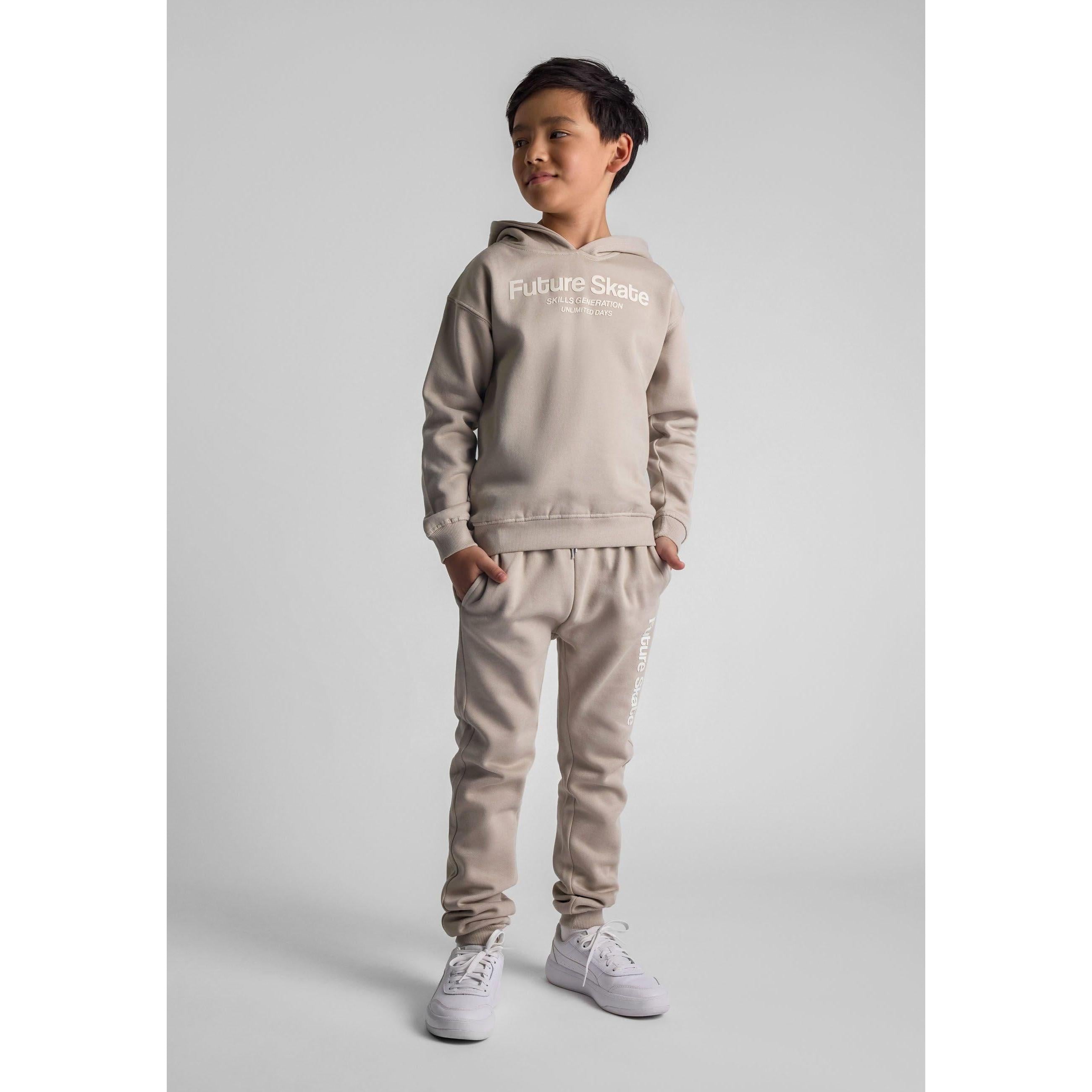 Young boy wearing grey Future Skate tracksuit set consisting of hooded sweatshirt and joggers, standing against white studio background