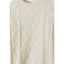 Close-up detail of cream cable knit jumper showing diamond texture pattern and crew neck collar with Minoti label