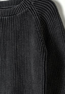 Detail of a boys' black cotton jumper with ribbed texture and raglan sleeves.
