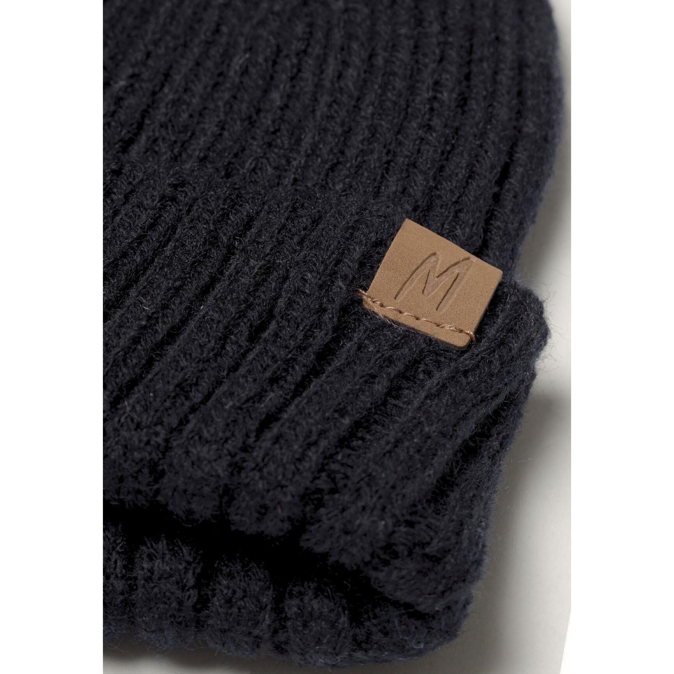 Close-up detail of black ribbed knit fabric texture showing brown leather M branded label attached to winter accessory