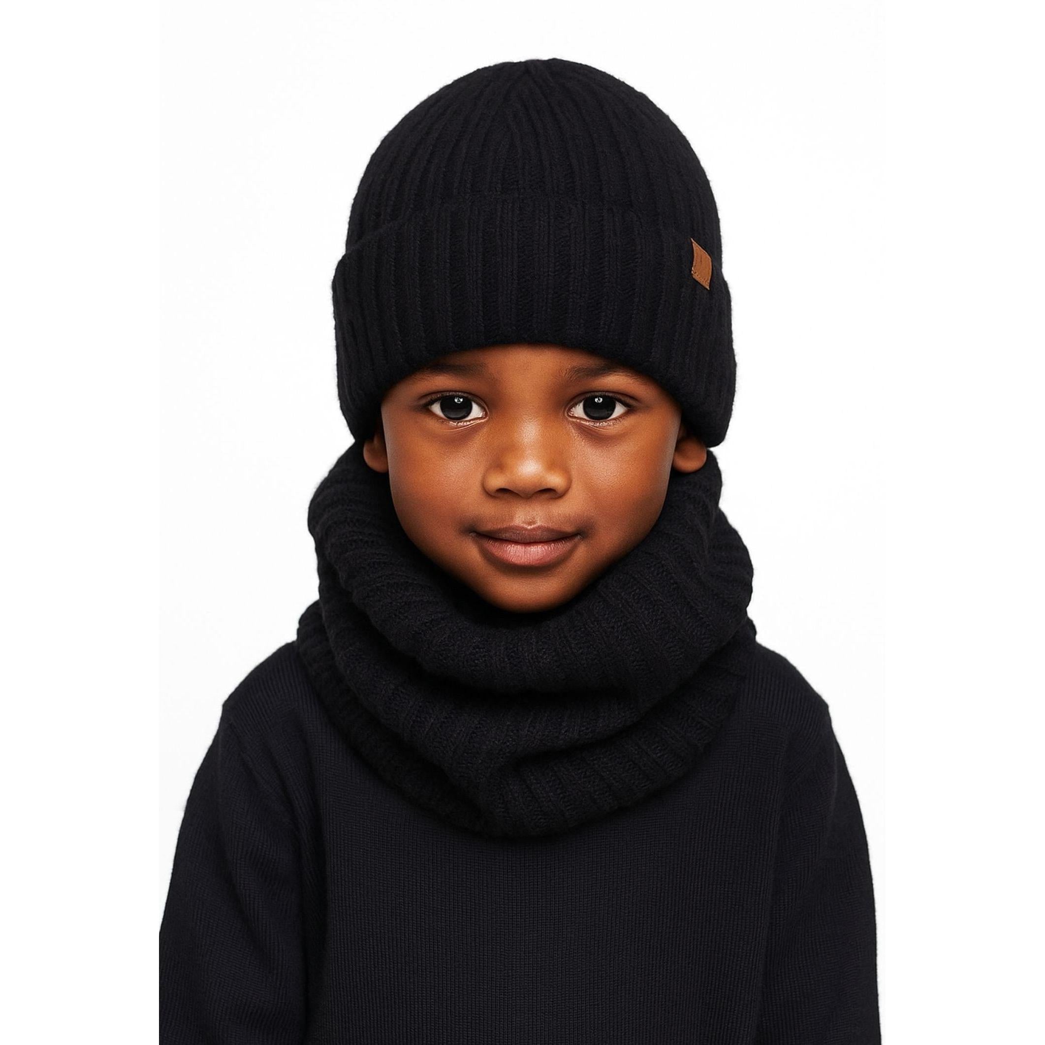 Young child wearing black ribbed knit beanie and snood set against white background, showing front view of winter accessories