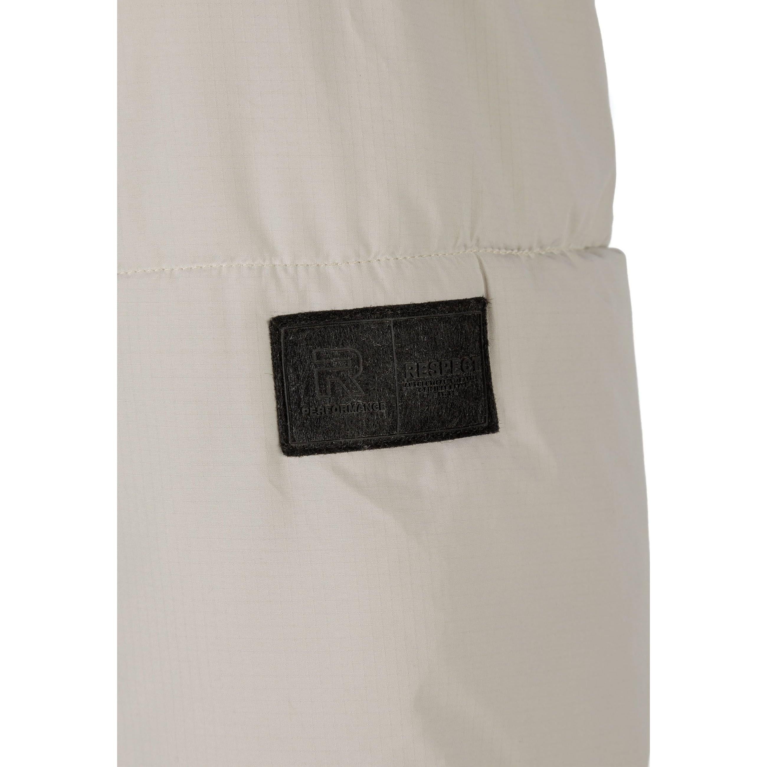 Close-up detail of black rectangular fabric label patch sewn on grey ripstop jacket sleeve showing textured fabric surface