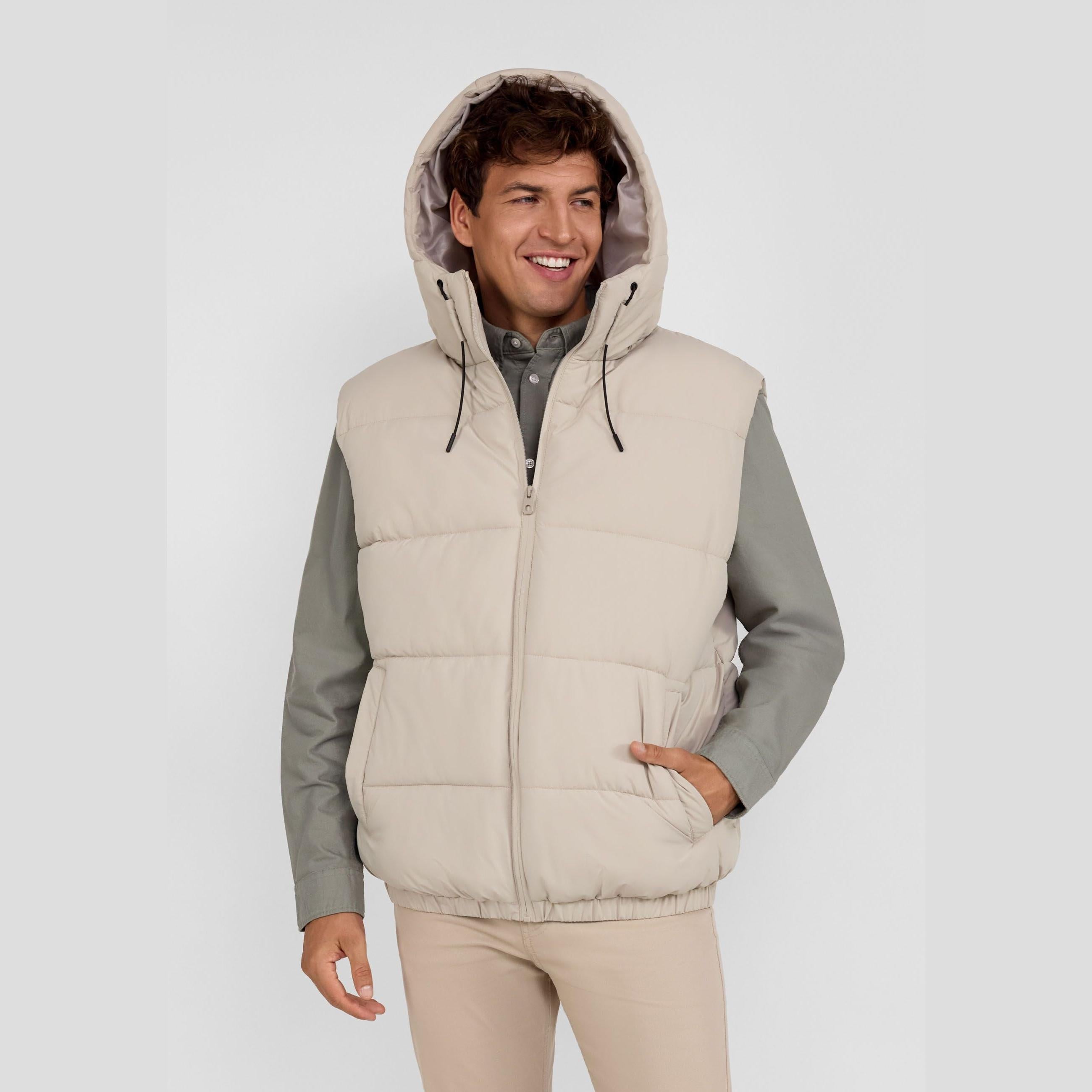Smiling man in a beige padded ripstop gilet with hood, full zip, and side pockets, over a grey shirt.