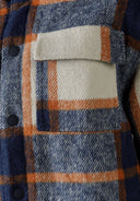 Detail of boys padded shirt jacket in blue check with orange accents, featuring a patch pocket.