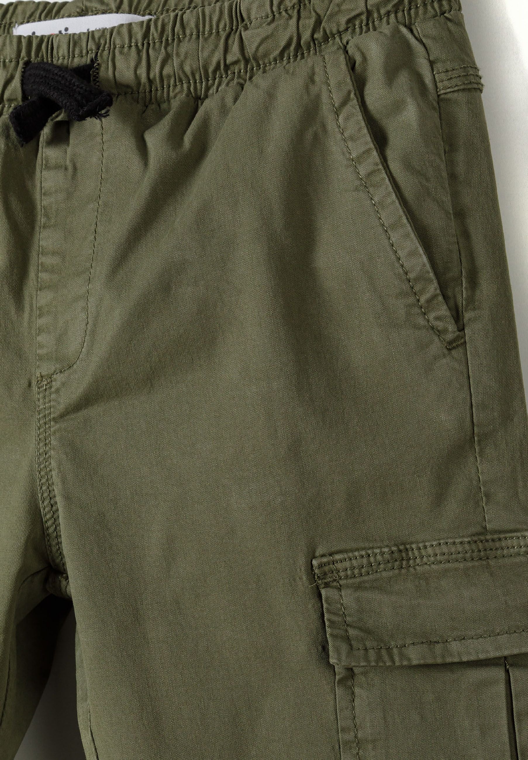 Detail of boys' khaki cargo trousers with elastic waist and side pockets.