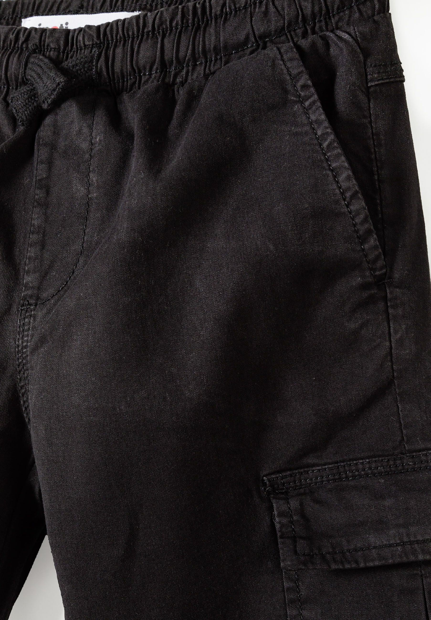 Close-up of black boys' cargo trousers with elastic waistband and side pockets.