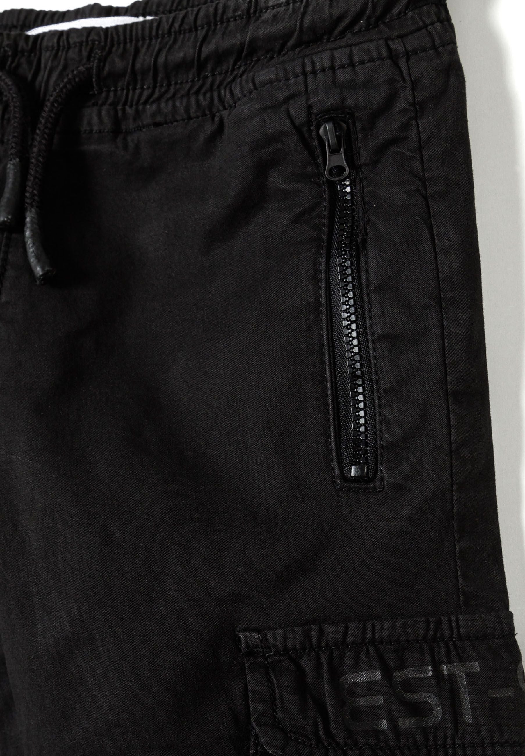 Close-up of black boys' cargo trousers featuring zippered front pocket and side print.
