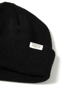 Close-up of a black ribbed beanie hat with a fold-up cuff and a logo badge.
