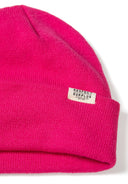 Detail of a pink ribbed beanie hat with a fold-up cuff and a logo badge.