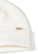 Detail of a white ribbed beanie hat with a cuff and a logo badge.