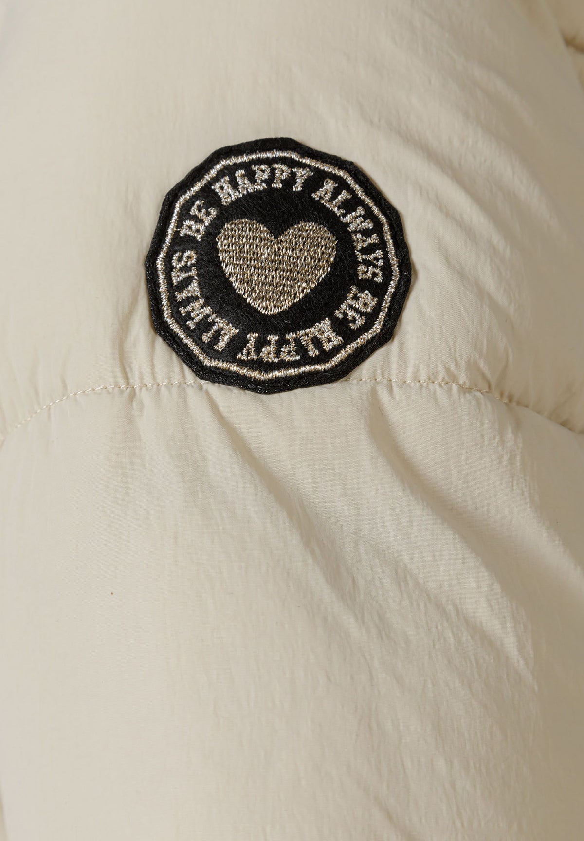 Close-up of the sleeve patch on the cream long puffer coat.